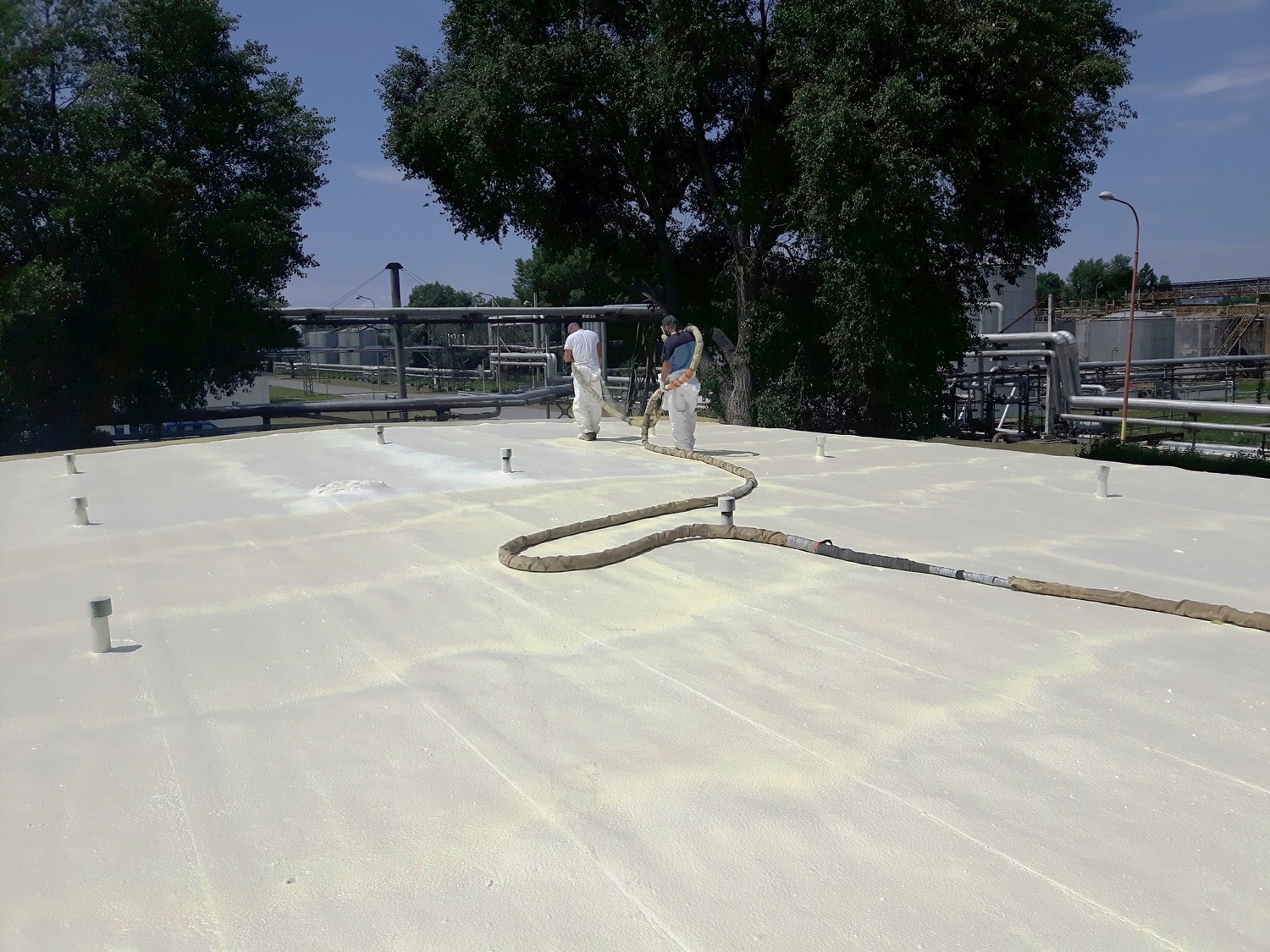 dva pracovníci v bílých pracovních kalhotech aplikující vrstvu izolačního materiálu na ploché střeše