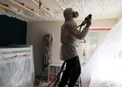 pracovník v bílém ochranném obleku s maskou nanášející izolační vrstvu na strop